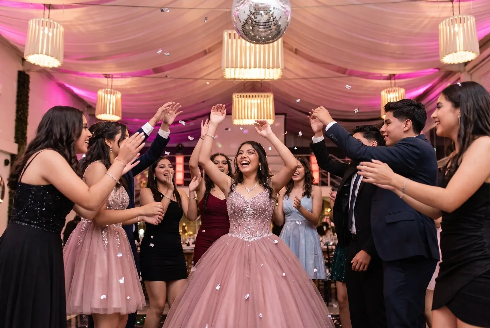 La quinceañera baila rodeada de sus amigos bajo las lámparas del salón