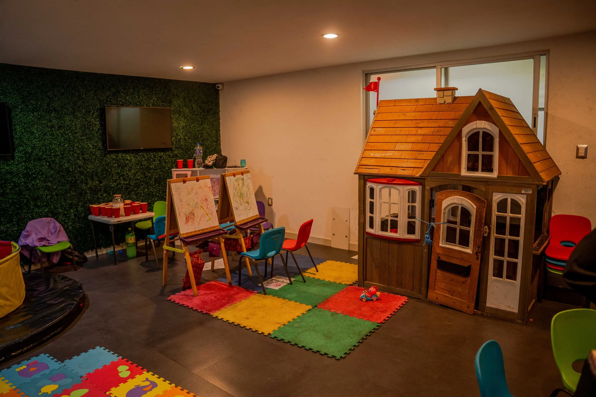 El cuarto de los niños, con una casita de madera, caballetes y tapetes de colores