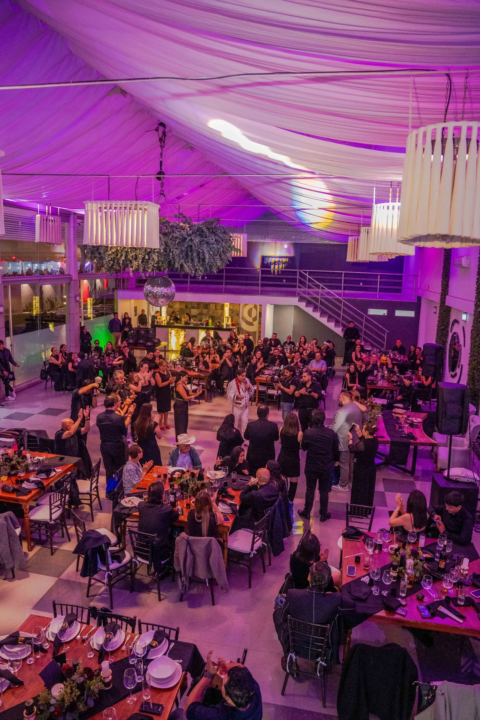 El salón de doble altura lleno de invitados, visto desde el mezzanine