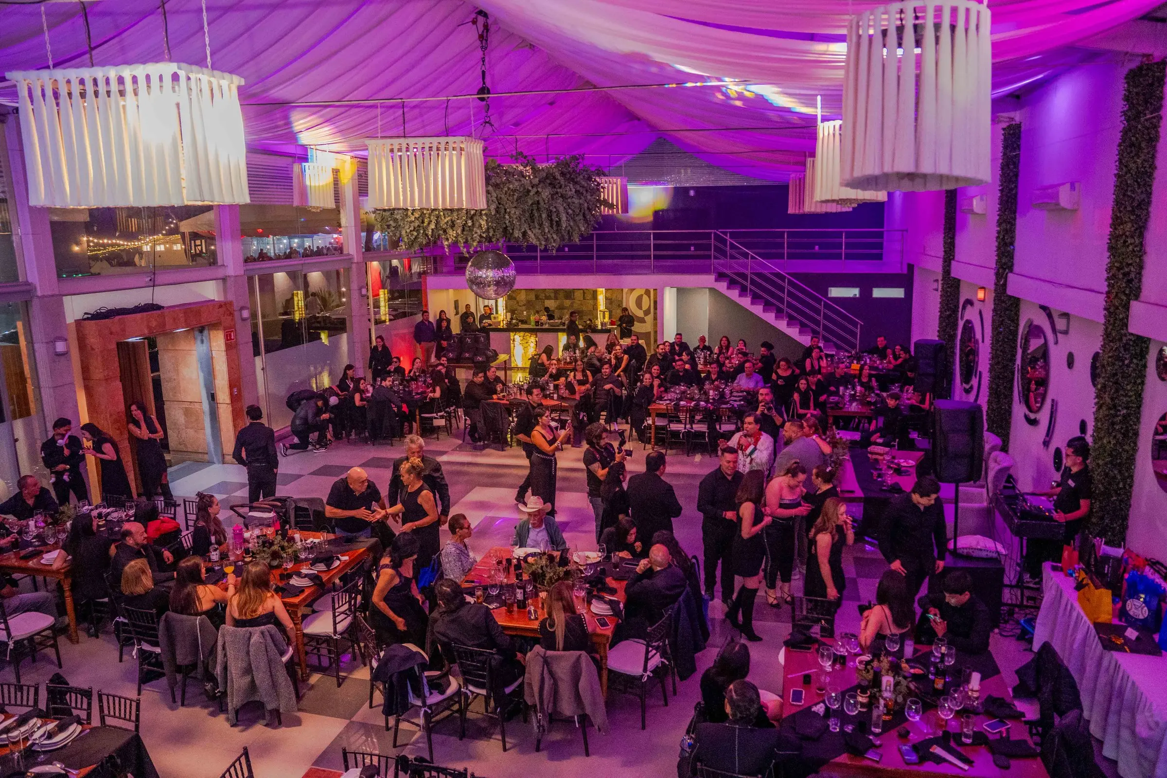 El salón lleno visto desde el mezzanine, con las mesas ocupadas y el techo de telas en luz violeta