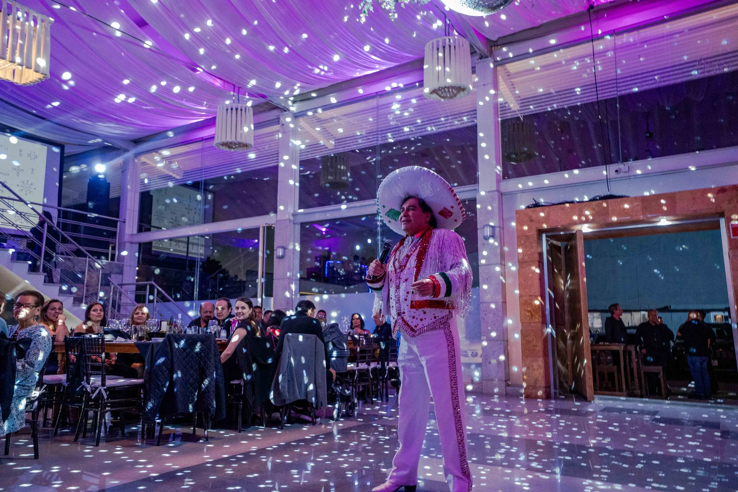Un cantante vestido de charro blanco en la pista de luces, con los invitados en sus mesas